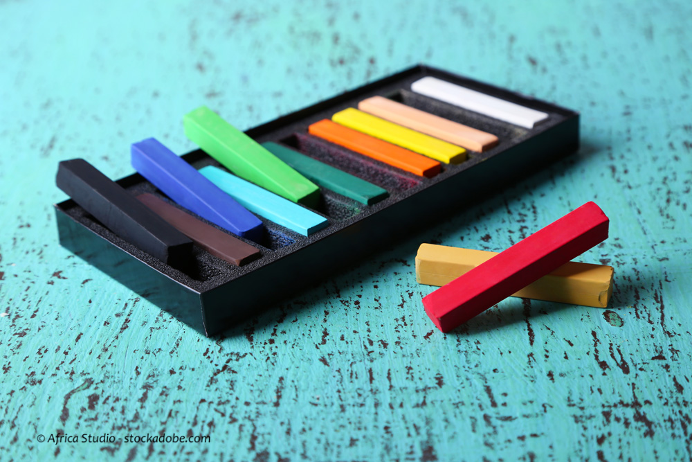 Colorful chalk pastels in box on color wooden background